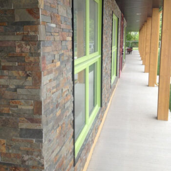 Exterior of a building with stacked stone walls and bright lime-green window frames along a long covered walkway.