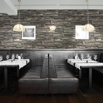 Restaurant dining area with dark leather booths, white tablecloths, and wine glasses against a stone accent wall with framed photos and pendant lights.