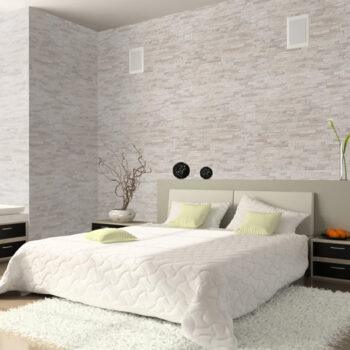 Contemporary bedroom with a tufted white quilt, pale yellow pillows, beige headboard, and a shag rug in front of the bed.