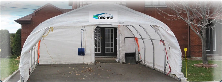 Abri Harnois XR18-XR20 - abri double résidentiel - Distribution DWP Abri Harnois XR18-XR20 installé devant une maison en brique, structure galvanisée et toile blanche 7 oz soudée, conçu pour deux voitures.